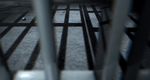 A jail cell with the bars casting shadows across the floor.