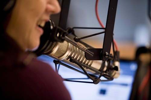 Smiling woman speaking into a professional-grade microphone in a studio.