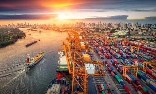 A photo illustration showing a busy shipping port with unloading cranes and a large number of shipping containers lined up on the dock.