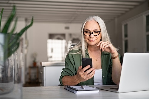 Happy senior woman using mobile phone while working at home.