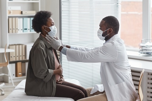 A black doctor checking the lymph nodes of a pregnant black female patient in his office.