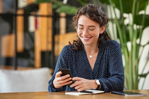 Young smiling business woman sending text message with smartphone.