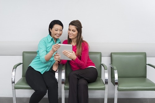 Smiling patient's using digital tablet while sitting at hospital.