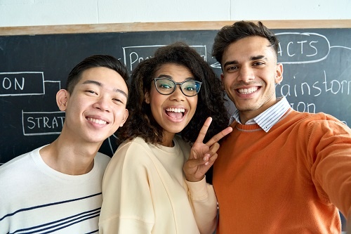 Three multicultural college students taking a selfie in front of a blackboard. 