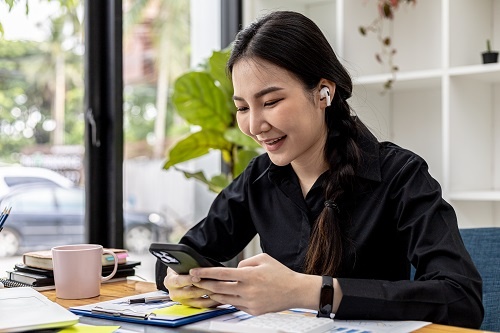 Businesswoman holding smartphone on desk with documents placed in front of her.