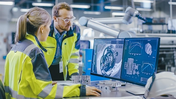 A woman looking at schematics on a computer screen on the floor of a manufacturing plant. 