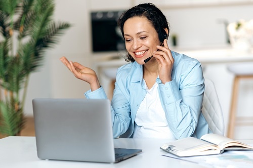 Friendly attractive woman in a headset communicates via video call on a laptop.